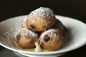 Puffy blueberry ricotta donuts are piled high, served atop lemon curd and dusted with powdered sugar.