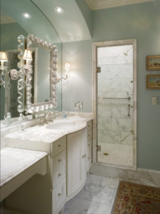 Pale blue walls, marble floors and white wood cabinetry come together to brighten up a spacious bath.